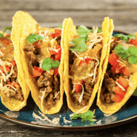 Four tacos with meat, cheese, and tomatoes.
