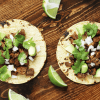Two tacos with meat, avocado, and cilantro.