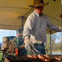 Man grilling meat under a tent.