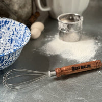 Wooden handled whisk on a counter.