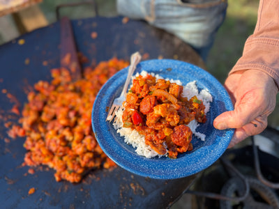 Jambalaya on a blue plate with rice, held over a wok with the rest of the jambalaya.
