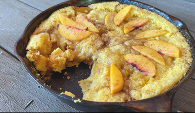 A sweet cornbread dump cobbler covered in peaches in a dutch oven