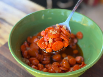 Hot Honey Glazed Cast Iron Carrots in a green bowl, held in a spoon
