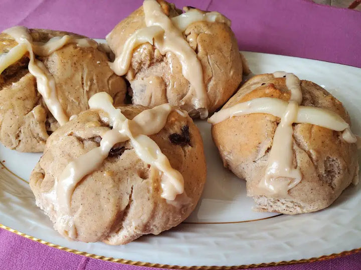 Four glazed hot cross buns on a plate.