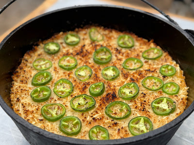 Image shows the top layer of a roasted dip covered with jalapeños, in a cast iron pan.