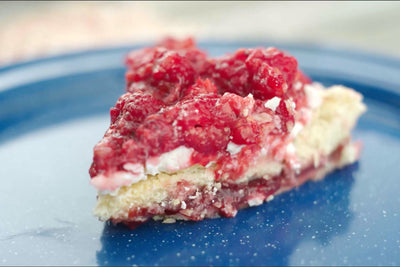 Close-up of White Chocolate Raspberry Bars with a flaky golden crust, creamy white chocolate filling, and fresh raspberries on a blue plate.
