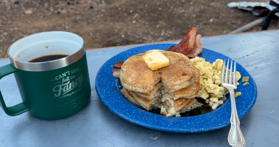 A cup of coffee in a "Can't Get Full on Fancy" yeti coffee mug and blue plate sourdough pancakes  dripping with maple syrup and butter