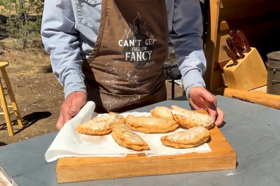 Cowboy Kent Rollins holds a cutting board with several golden fried apple and apricot pies on top 