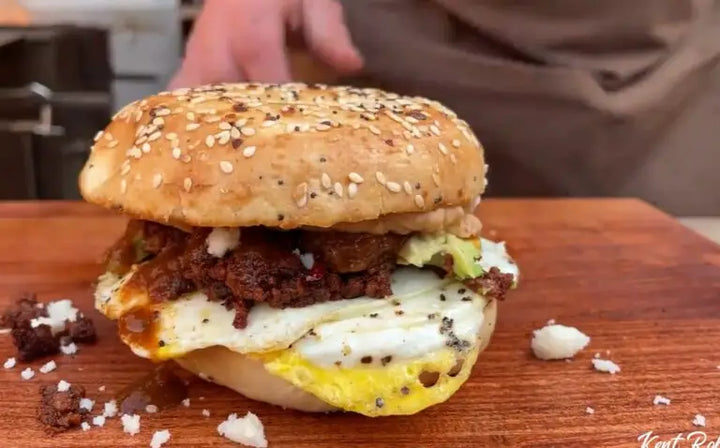 A hamburger with an egg on it sitting on top of a wooden board.