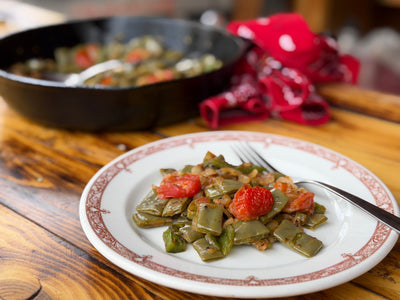 Nopales a la Mexicana on a white plate, placed on a cutting board, with a cast iron skillet in the background