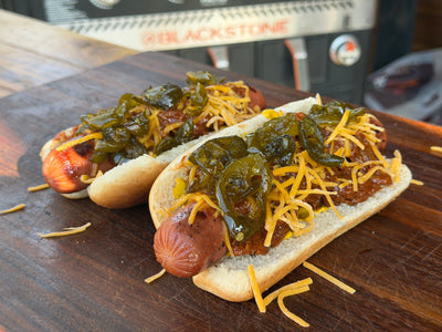 Two hot dogs on buns with brisket, candied jalapeno, and shredded cheddar cheese