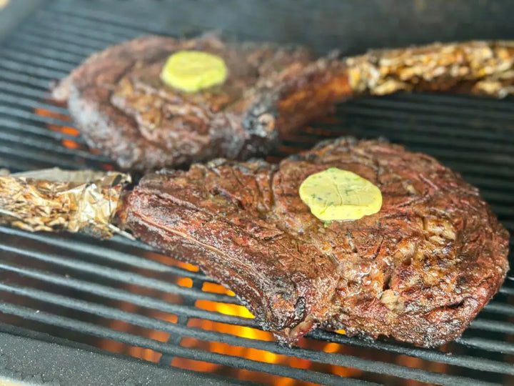 Two grilled tomahawk steaks with butter.