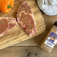 Seasoned steaks on cutting board with seasoning.