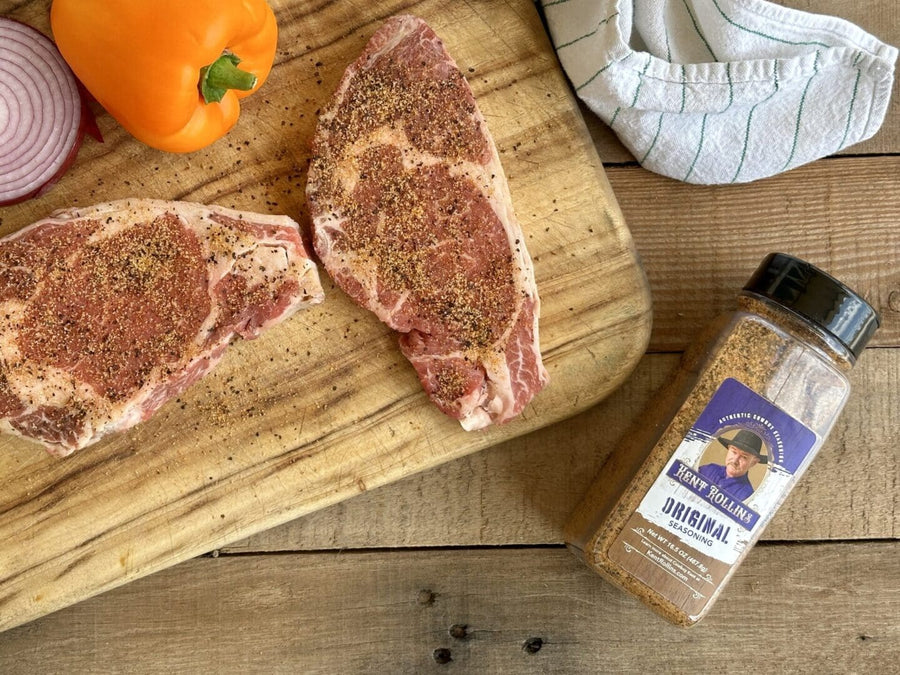 Seasoned steaks on cutting board with seasoning.