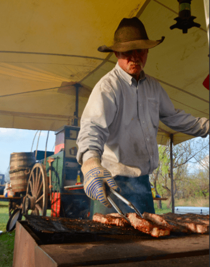 Man grilling meat under a tent.