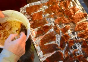 Hands dipping meat in marinade on tray.