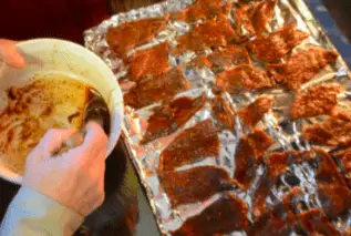 Hands dipping meat in marinade on tray.