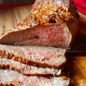 Sliced roasted beef with knife on wood board.