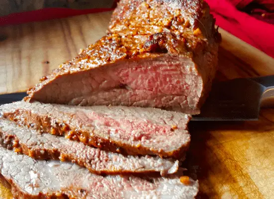 Sliced roasted beef with knife on wood board.