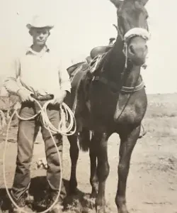 A cowboy stands with his horse and lasso.