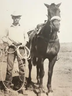 A cowboy stands with his horse and lasso.