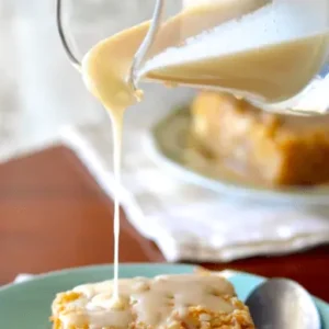 Creamy sauce being poured over cake.