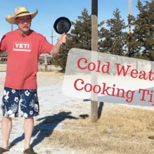 Man in shorts cooking outdoors in the snow.