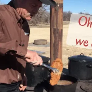 Man cooking food outdoors with a sign.