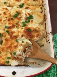 Cheesy casserole with green onions and a wooden spoon.