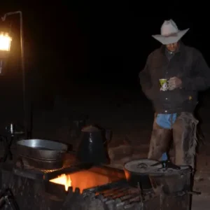 Cowboy warming himself by a campfire.