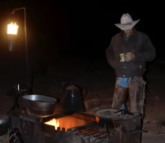 Cowboy warming himself by a campfire.