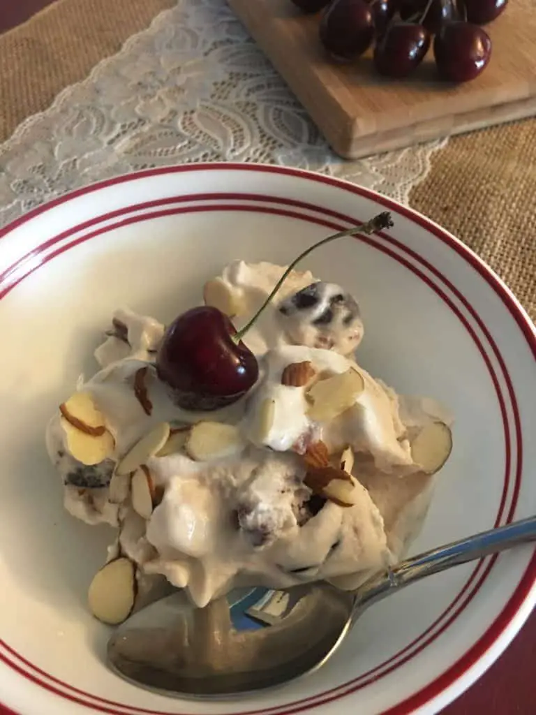 Ice cream with cherry and almonds in bowl.