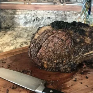 Roasted prime rib with knife on cutting board.