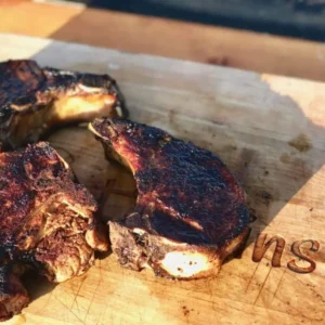 Three grilled pork chops on a wooden board.