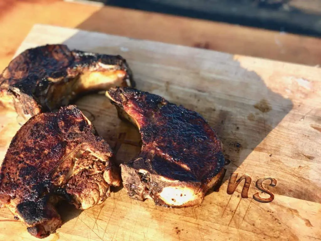 Three grilled pork chops on a wooden board.