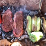 Steak and vegetables grilling over hot coals.