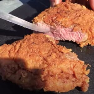 A crispy fried steak being cut with a knife.