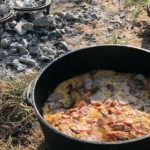 A Dutch oven filled with food over coals.