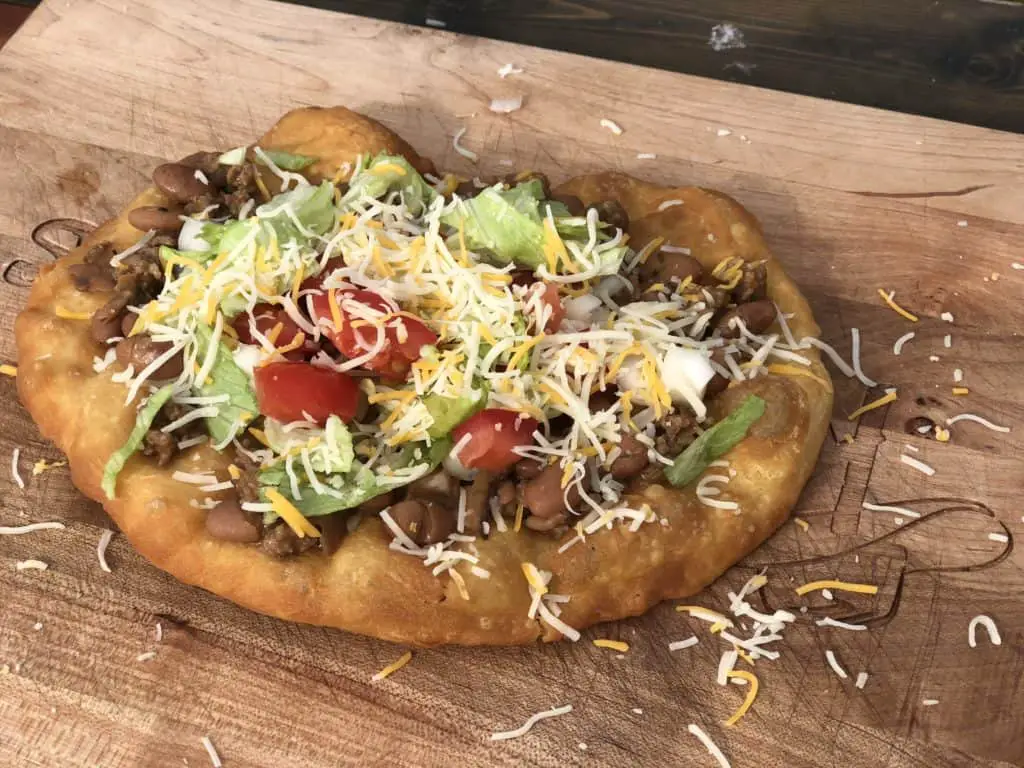 Fried bread topped with meat, cheese, lettuce, and tomatoes.