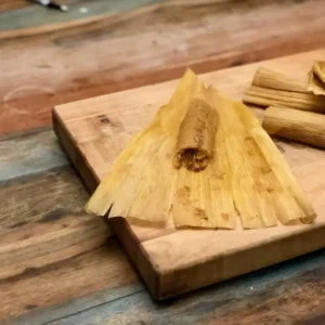 Corn husk tamales on a cutting board.