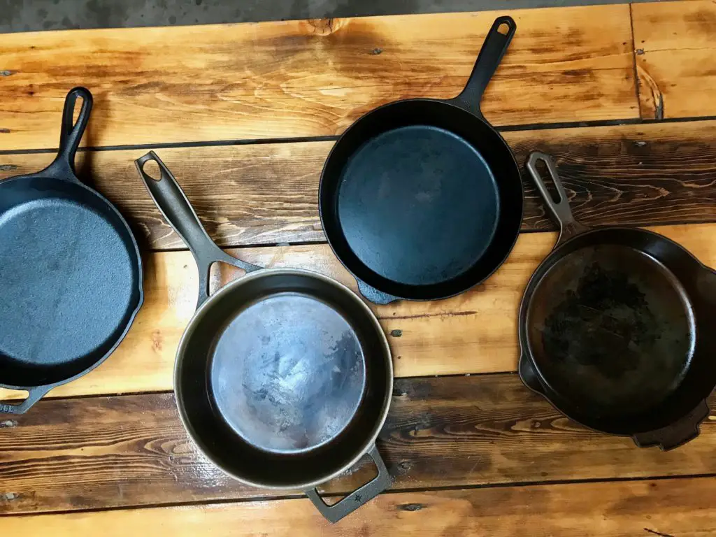 Four cast iron skillets on wood table.