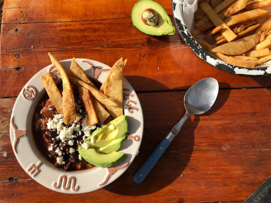 Bowl of chili with avocado and chips.