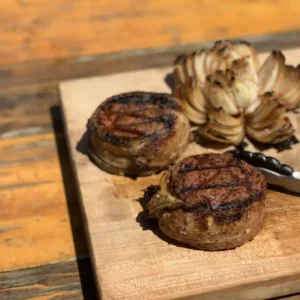 Bacon-wrapped steak with onion rings on wood board.