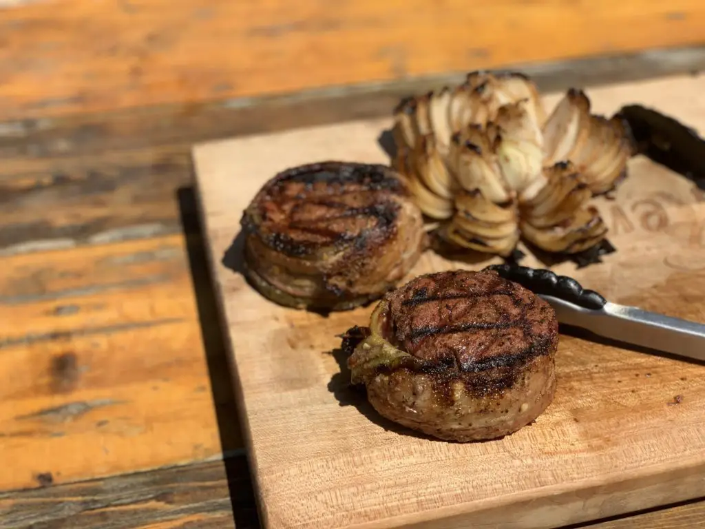 Bacon-wrapped steak with onion rings on wood board.