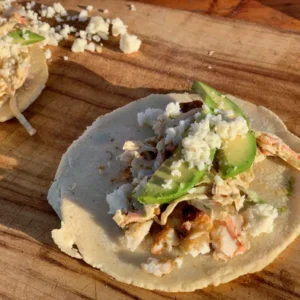 Two tacos with avocado, cheese, and seafood.