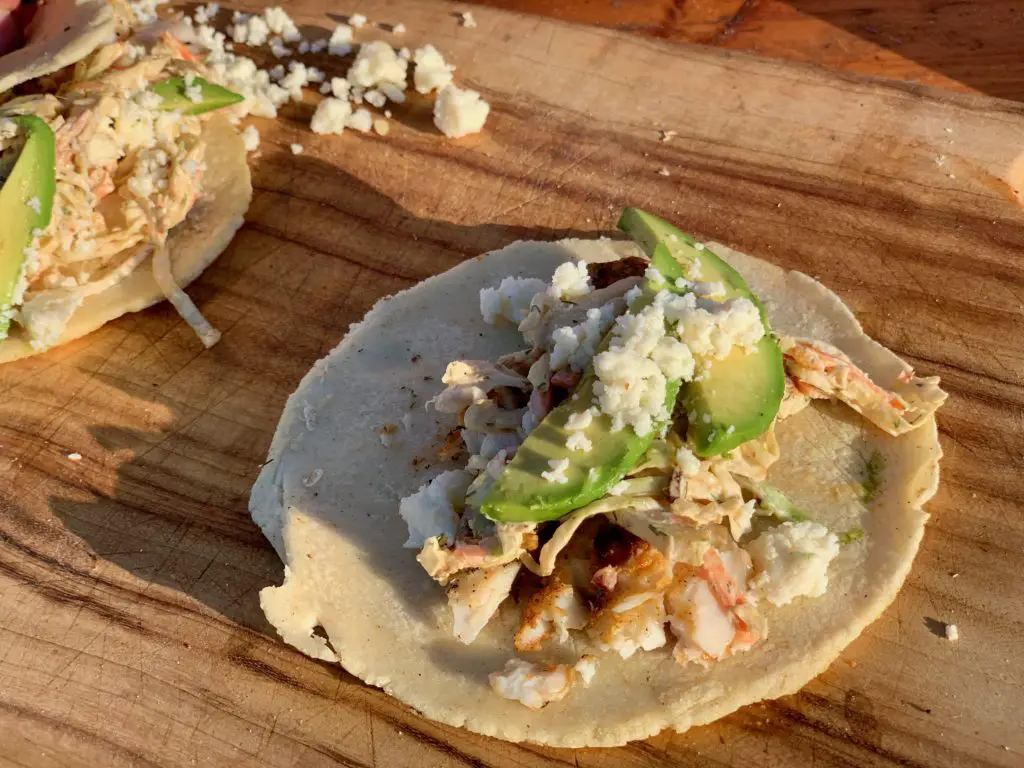 Two tacos with avocado, cheese, and seafood.