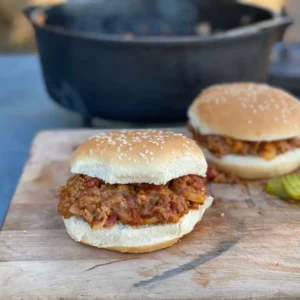 Two sloppy joe sandwiches on a cutting board.