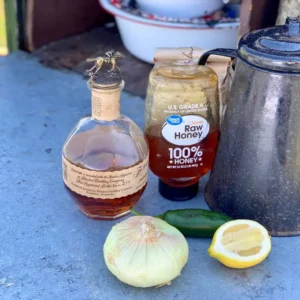 Whiskey, honey, lemon, and onion on table.