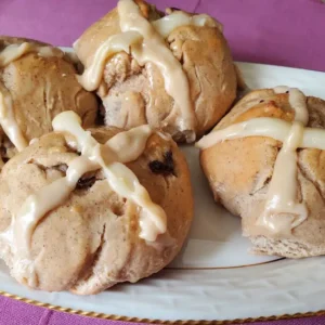 Four glazed hot cross buns on a plate.