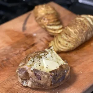 Baked potatoes with butter on wooden board.